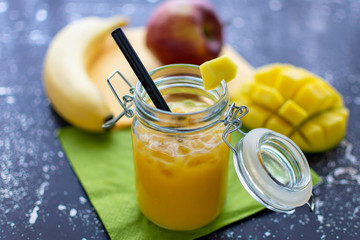 leckerer Smoothie mit Mango im Einmachglas mit Strohhalm und crushed ice. Im Hintergrund liegen frische Früchte