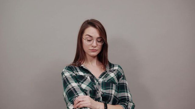 Young brunette girl blue green in checked shirt on grey background happy woman with glasses rolls up her sleeves and smiles