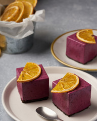 raw currant cheesecake a square cake with a slice of dried orange on a gray concrete background
