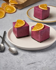 raw currant cheesecake a square cake with a slice of dried orange on a gray concrete background