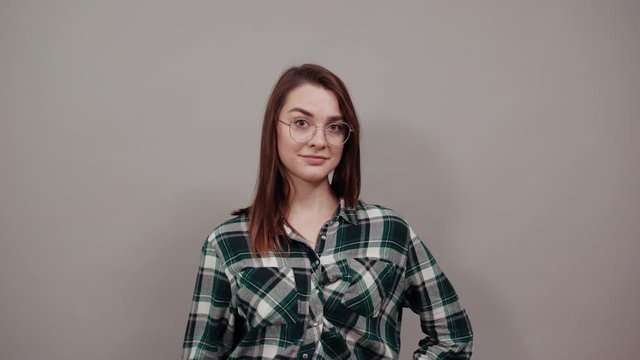 Young brunette girl blue green in checked shirt on grey background confident woman in glasses shows four fingers