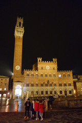 Fototapeta na wymiar Siena by night. Piazza del Campo and Tower del Mangia illuminated..Tourists in the square.