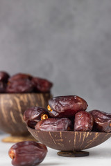 Coconut shell with organic medjool dates on a light grey concrete background. Selective focus, copy space.