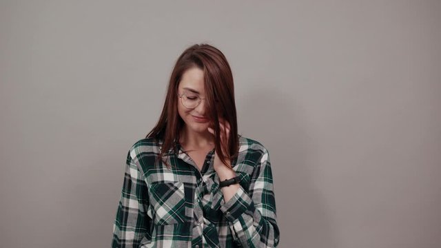 Young brunette girl blue green in checked shirt on grey background upset woman in glasses with bad mood