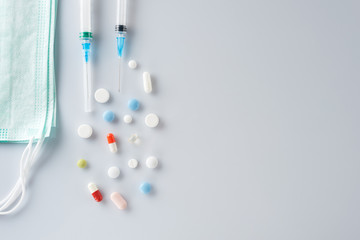 Disposable face masks,syringes and scattered pills on a light gray  background.
