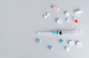 Medicine pills and syringe on gray background.