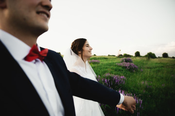 the groom in the foreground,bride and groom hugging at sunset.Happy bride and groom smiling.Happy bride and groom after the wedding ceremony.Wedding day.Beautiful young couple in a field with flowers