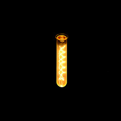 Antique burning light bulb with a tungsten filament glowing in complete darkness