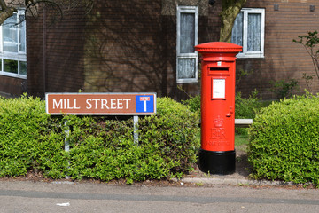 Fototapeta na wymiar Street Sign & Red Posting Box at side of Road between Green Hedge 