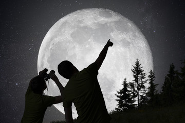 Silhouettes of people observing stars in night sky. Moon in back