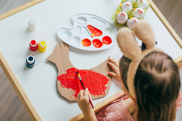 Top view of little girl with bunny ears painting paper hen