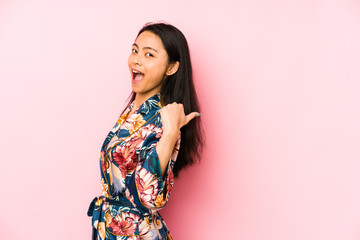 Young chinese woman wearing a asiatic pijama isolated smiling and pointing aside, showing something at blank space.