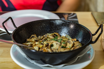 On the dining table is a hot pan with champignons in garlic sauce. horizontal view, closeup. Selective center focus and blurred foregraund