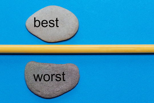 The words best and worst are written on natural smooth stones separated by a yellow pencil. The background is isolated in blue and has a lot of space