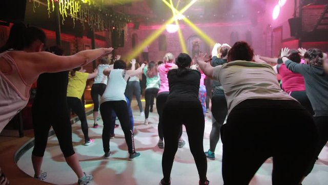 A large group of people are engaged in fitness with free entrance to the night club, play sports with music and concert lighting