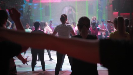 A large group of people are engaged in fitness with free entrance to the night club, play sports with music and concert lighting