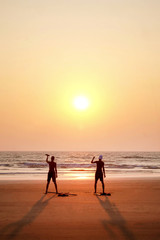 Fototapeta na wymiar two unrecognizable men excerscising at sunset by holding small weights on a deserted beach