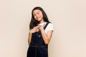 Young cute chinese teenager Young blonde woman wearing a coat against a pink background laughs out loudly keeping hand on chest.