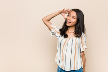 Young cute chinese teenager Young blonde woman wearing a coat against a pink background looking far away keeping hand on forehead.