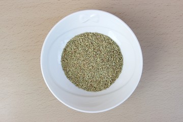 Ground rosemary in a white ceramic bowl isolated on a wooden table from above. Soft focus at the background