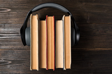 Headphones worn on a stack of old books on wooden background. Favorite audiobook concept. Top view