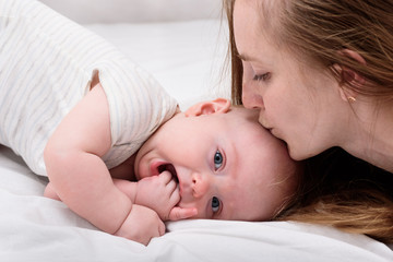 Young mother kissing baby lying on bed, close up. Lovely time together. Happy motherhood concept