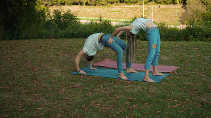 Young flexible man and woman having stretching yoga morning class exercising together in the park. Physical and mental health concept.