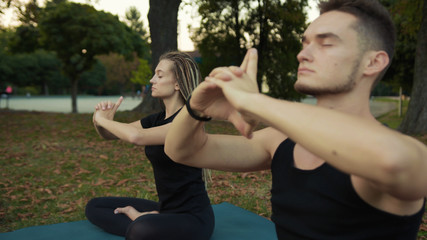 Hipster young man and woman practising yoga prayer stretching together in the morning outside in beautiful park. Meditation concept.