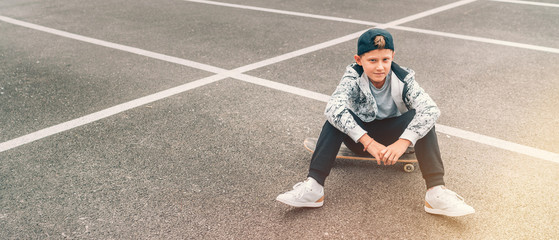 Teenager skateboarder boy with a skateboard sitting on asphalt playground and resting after he made tricks. Youth generation Freetime spending concept image. © Soloviova Liudmyla