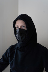 Portrait of a man defending himself from a coronavirus with a medical mask, dressed in black clothes on a light background. Flu pandemic covid 19