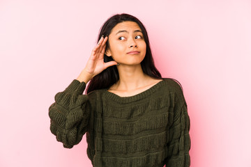 Young chinese woman isolated on a pink background trying to listening a gossip.