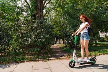 Naklejka premium Woman rides on electric scooter along sunny street