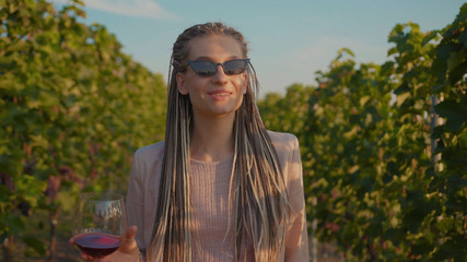 Portrait face young woman stand the vineyards with glass of red wine tasting smile feel happy organic connecting with nature agriculture sunny travel countryside grape field green rural slow motion