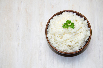steamed rice in a Cup on a wooden white table and a parsley leaf selective