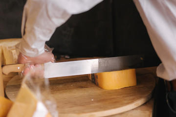 Man slicing a cheese on wooden board. Cheese shop