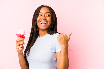 Young african american woman holding an ice cream isolated points with thumb finger away, laughing and carefree.