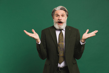Bearded middle-aged man in khaki suit waving his hands to the side on a green background with copy space.