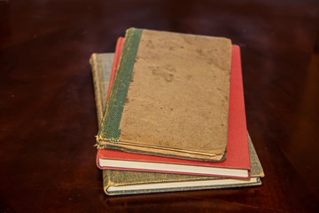 Three old discolored hardback books laying stacked on dark brown surface with foreground - bottoms of books in clear focus and tops blurred out