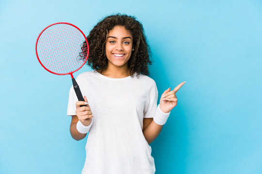 Young african american woman playing badminton smiling and pointing aside, showing something at blank space.