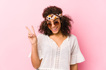 Young african american hipster woman isolated on pink background joyful and carefree showing a peace symbol with fingers.