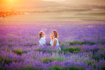 Mom and daughter in beautiful white dresses in a lavender field in the summer at sunset.