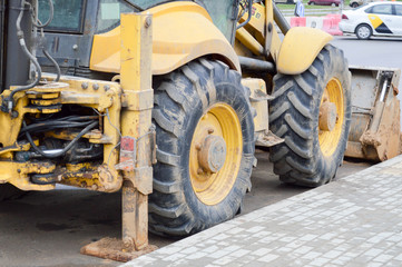 Obraz premium Big bright yellow powerful industrial heavy excavator tractor, bulldozer, specialized construction equipment for road repair during the construction of a new micro-district in a big city
