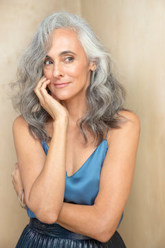 A youthful looking middle-aged woman with grey hair looks off camera, with one hand up to her face., Studio City, CA, USA