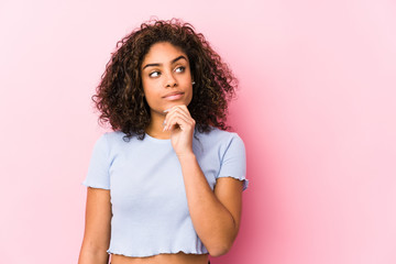 Young african american woman against a pink background looking sideways with doubtful and skeptical expression. - obrazy, fototapety, plakaty