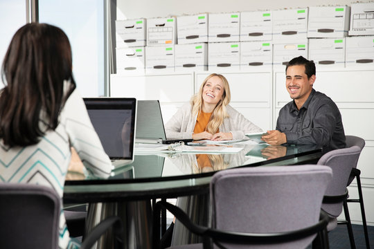 Three co-workers talk while on their computers and tablets., Jacksonville, Florida, USA