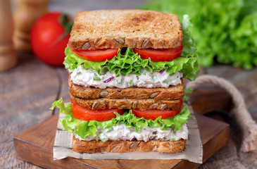 Stack of tuna salad sandwich on multigrain bread with tomato, lettuce and mayonnaise on wooden board. Rustic wooden background.  Selective focus.