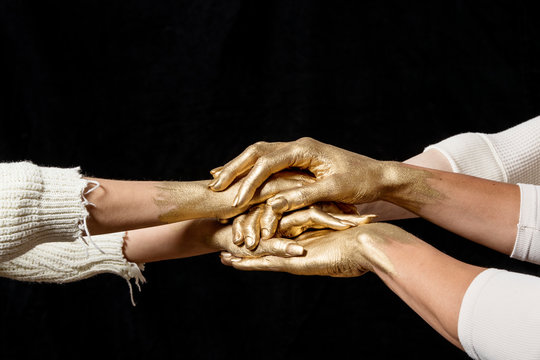 Close-up shot of group's gold painted hands on top of another against black background., Dallas, Texas, USA