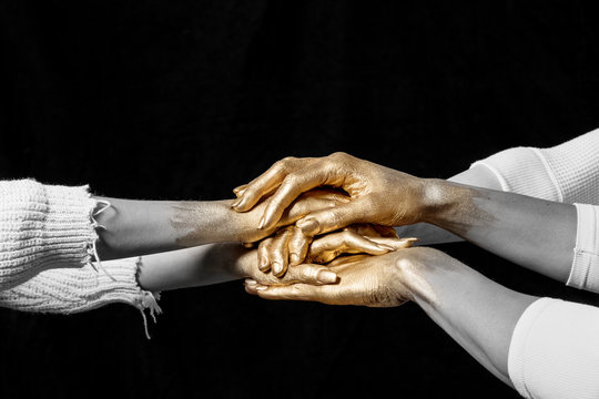 Desaturated/close-up shot of group's gold painted hands on top of another against black background., Dallas, Texas, USA
