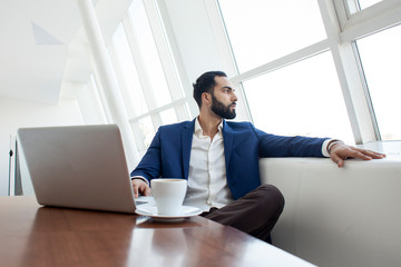 young successful businessman use a laptop and drink coffee in the morning at work, a freelancer is sitting with a computer in a white cafe