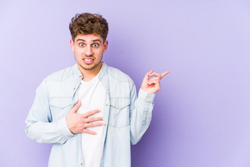 Young blond curly hair caucasian man isolated shocked pointing with index fingers to a copy space.
